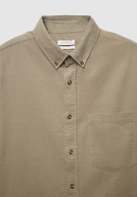 Chemise beige boutonnée avec col, en tissu de coton texturé, dotée d'une poche poitrine et de boutons marron sur le devant.