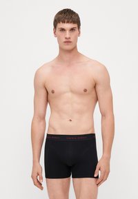Schwarze Boxershorts mit einer taillierten Passform, ausgestattet mit einem weichen Bund, der mit "JACK & JONES" in Rot beschriftet ist; glatte Textur und minimalistischer Stil.