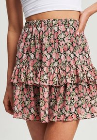 Květinová sukně s černým pozadím, zdobená růžovými a zelenými vzory, ve vrstvených volánech a s elastickým pasem pro pohodlné nošení.