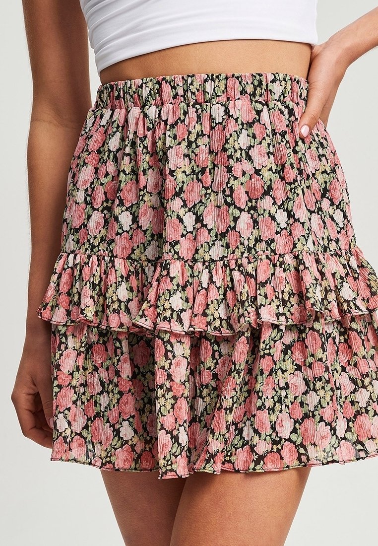 Květinová sukně s černým pozadím, zdobená růžovými a zelenými vzory, ve vrstvených volánech a s elastickým pasem pro pohodlné nošení.