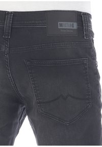 Jeans in denim nero con una tasca posteriore decorata da un design a onda cucito e un'etichetta rettangolare con la scritta "MUSTANG True Denim."