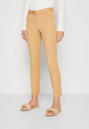 Beige tailored pants met slim fit, glad textiel, zijzakken en een bijpassende riem. Gekleed met lichtgekleurde gevlochten instapsandalen.