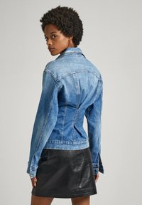 Denim jacket with a fitted design, light blue color, pointed collar, and button details, paired with a black leather skirt.