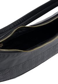 Sort læderhåndtaske med tekstureret nederste panel og guld lynlås. Åben top, der viser et sort inderskud. To lange, flade håndtag.