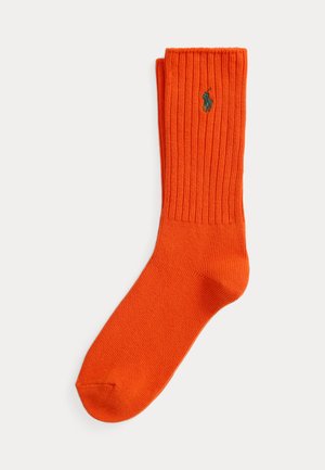 Chaussette montante côtelée orange vif avec un petit logo brodé vert foncé représentant un cheval et un cavalier sur la partie supérieure du mollet.