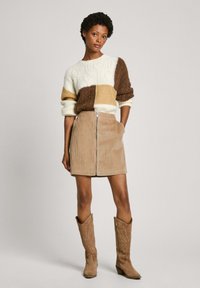 Maglione a maglia con blocchi a motivo in crema, marrone e sabbia; abbinato a una mini gonna in corduroy sabbia con cerniera frontale e tasche; stivali marroni.