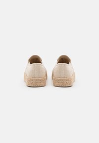 Scarpe slip-on in tela beige con suola in juta texturizzata, caratterizzate da un design semplice e una parte posteriore arrotondata con dettagli di cucitura minimi.