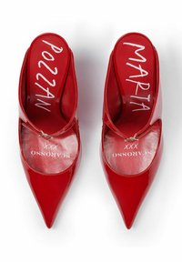Mule in pelle verniciata rossa con punta affusolata; presenta un retro aperto e un cinturino decorativo con un accento metallico. Testo stampato sulle solette.