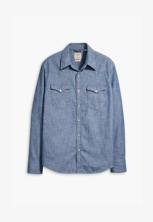 Chemise en chambray bleu clair à manches longues, col pointu, deux poches poitrine et boutons-pression argentés. Texture lisse avec un design classique.