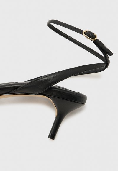 Μαύρο δερμάτινο slingback γοβάκι με χαμηλό τακούνι kitten, χρυσό λουράκι με αγκράφα, μυτερή μύτη και λεία σόλα σε λευκό φόντο.