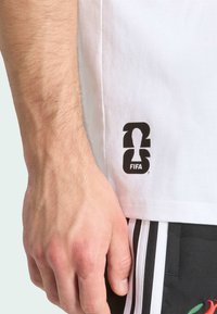 Camiseta blanca con un logo negro de FIFA y un gráfico de "23" en el lado inferior, combinada con pantalones cortos negros con rayas blancas a los lados.