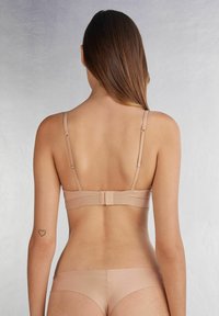 Nude lingerieset met een eenvoudige bh met verstelbare bandjes, een haaksluiting en bijpassende bikini slipjes in een zachte, gladde stof.