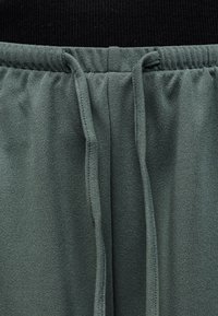 Κοντινή λήψη γκρι ελαστικής μέσης με δεμένους υφασμάτινους κορδόνια σε υφασμάτινο μαλακό παντελόνι με υφή.