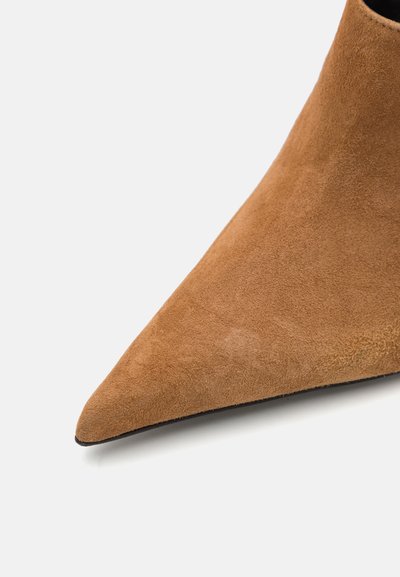 Brun mockaskinnssko med spetsig tå och en slät yta samt en snygg design, med en svart sula. Skons form smalnar av skarpt mot framsidan.