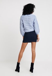 Světle modrý pletený svetr s texturovaným kabelovým vzorem, kombinovaný s námořnickou úzkou sukní. Černé vysoké kotníkové boty dokončují outfit.