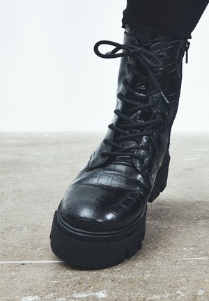 Botín negro de cuero hasta el tobillo con textura de cocodrilo, puntera redonda, suela de plataforma robusta y diseño con cordones en la parte frontal que incluye una cremallera lateral.