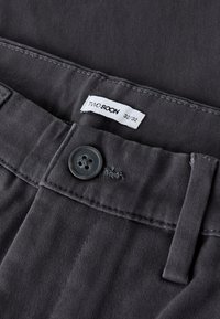 Gray cotton trousers with a button closure, featuring a label reading "TWO SOON" and size 32/32, showcasing a smooth, textured fabric.