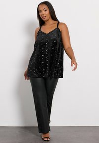 Svart sammetslinne med stjärndekorationer, V-ringning och tunna remmar, kombinerat med svarta läderbyxor och klacksandaler.