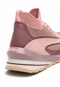 Zapatilla deportiva rosa con parte superior de malla texturizada, detalles lisos de cuero y una suela de cuña que presenta una franja y una marca de contraste.