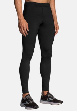 Zwarte sportlegging met een gladde, rekbare stof, voorzien van een hoge tailleband en een aansluitend ontwerp. Gecombineerd met donkere hardloopschoenen.