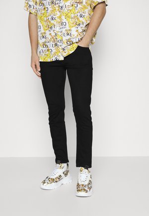 Pantalones negros ajustados combinados con una camisa de manga corta de estampado multicolor que presenta patrones florales y de texto. Zapatillas blancas con un diseño floral.