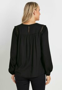 Blusa nera a maniche lunghe con spalle arricciate, chiusura con bottoni sul retro e dettagli arricciati per una vestibilità comoda. Tessuto morbido.