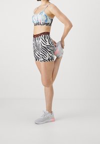 Jasnoniebieski sportowy stanik, czarno-białe szorty w zebra wzór z pomarańczowym obszyciem oraz szare buty sportowe z różowymi akcentami.