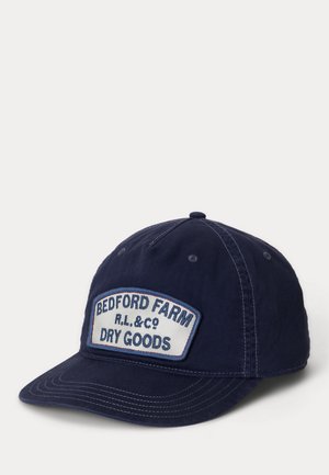 Granatowa czapka z daszkiem z białą naszywką z napisem "BEDFORD FARM R.L. & CO DRY GOODS" na przednim panelu.