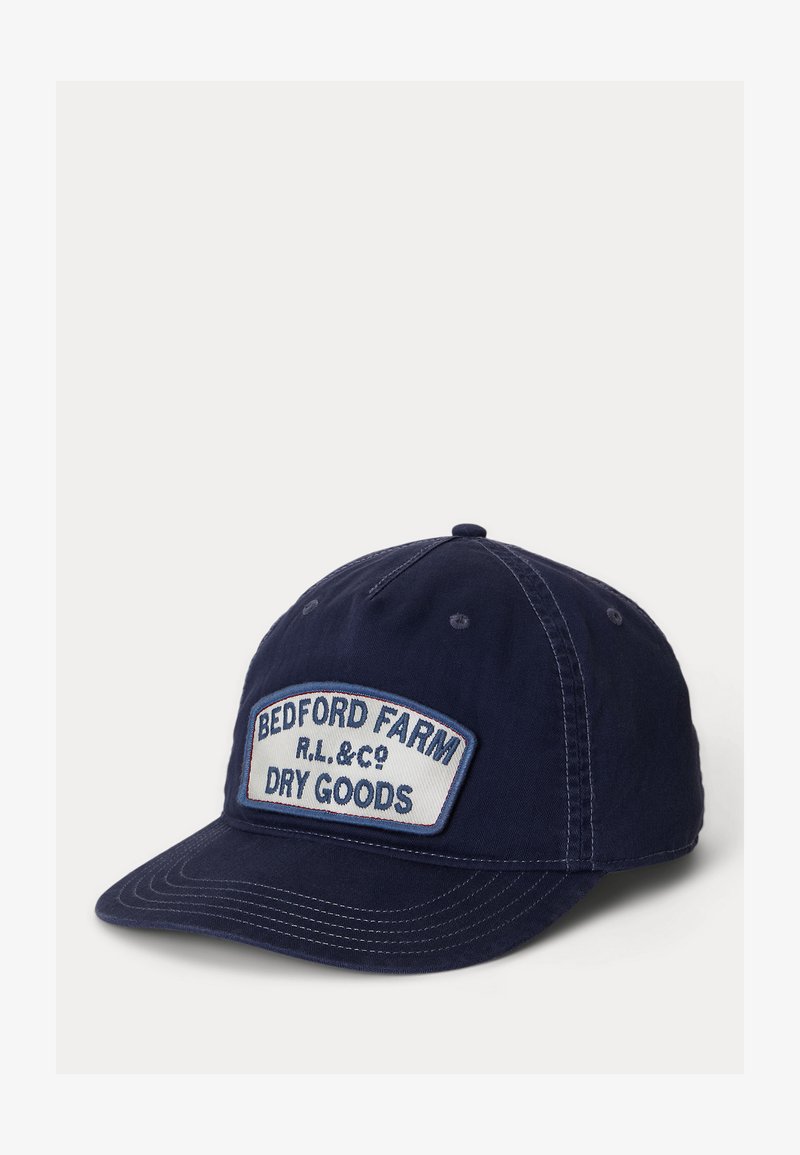 Καπέλο μπέιζμπολ σε σκούρο μπλε χρώμα με λευκή μπαλώματος που γράφει «BEDFORD FARM R.L. & CO DRY GOODS» μπροστά.