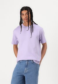 Purple cotton t-shirt with a crew neck and short sleeves. Features a small white Nike logo on the chest. Worn with blue denim jeans.