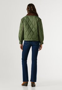 Quilted olive green jacket with a brown corduroy collar, featuring a relaxed fit and stitched detailing, paired with dark blue flared jeans.