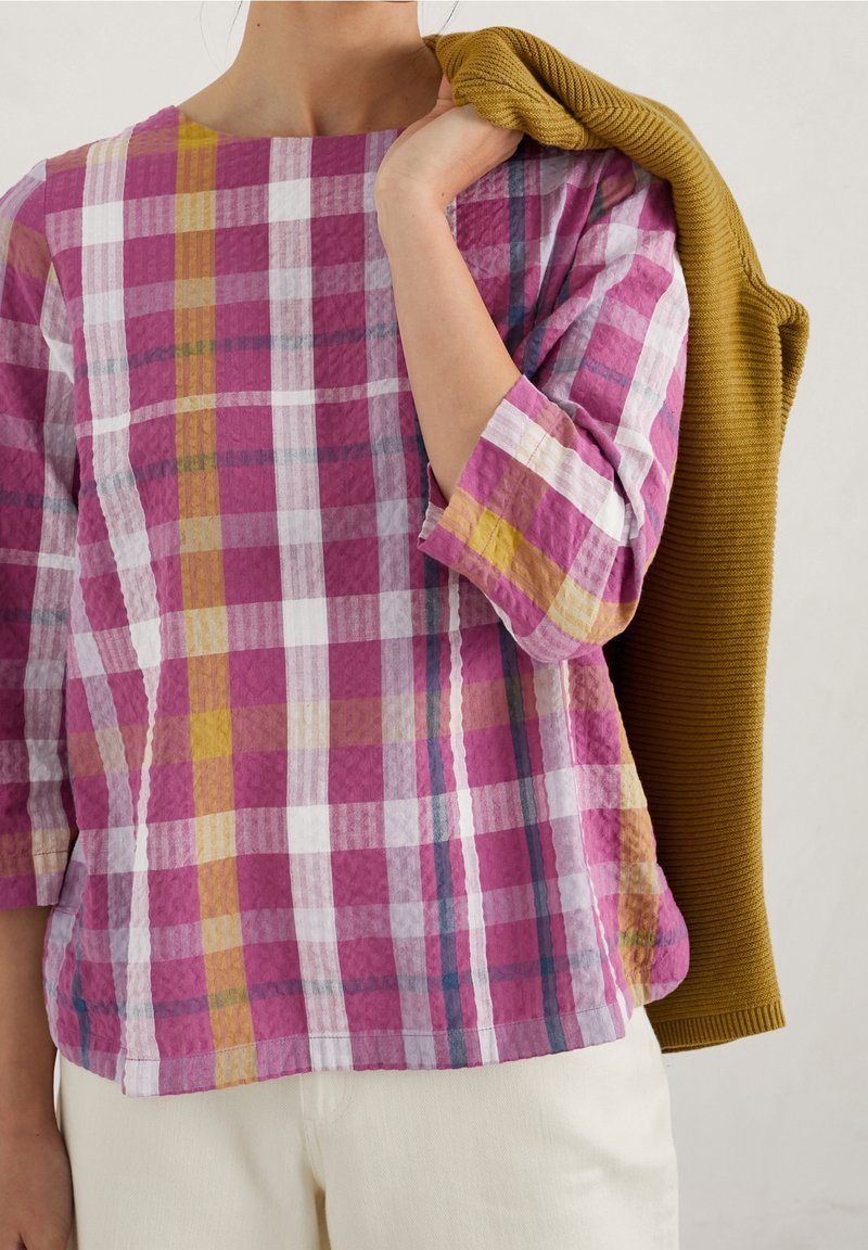 Purple and white checkered top with three-quarter sleeves, textured fabric, complemented by a mustard sweater draped over the arm.