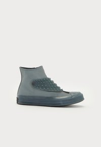 Shoe de cano alto feito de borracha translúcida, numa cor teal suave com accents de padrão de estrelas na lateral e bico arredondado.