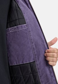 Purple jacket interior featuring a quilted black lining, pockets, and visible stitching. Zipper on the side. Textured fabric.