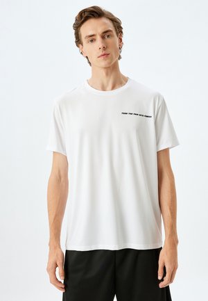Camiseta blanca de manga corta hecha de un material suave y liviano. Presenta un gráfico de texto en negro: "CONVIERTE EL DOLOR EN PODER" en el pecho.