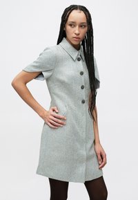 Kortärmad fiskbensmönstrad klänning i ljusblått och krämvitt. Den har knappslå framtill och en spetsig krage. Skräddarsydd passform med sidofickor.