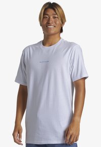 Camiseta de algodón blanca con mangas cortas, que presenta un pequeño logo azul en el pecho. Ajuste estándar, textura suave y diseño de cuello redondo.