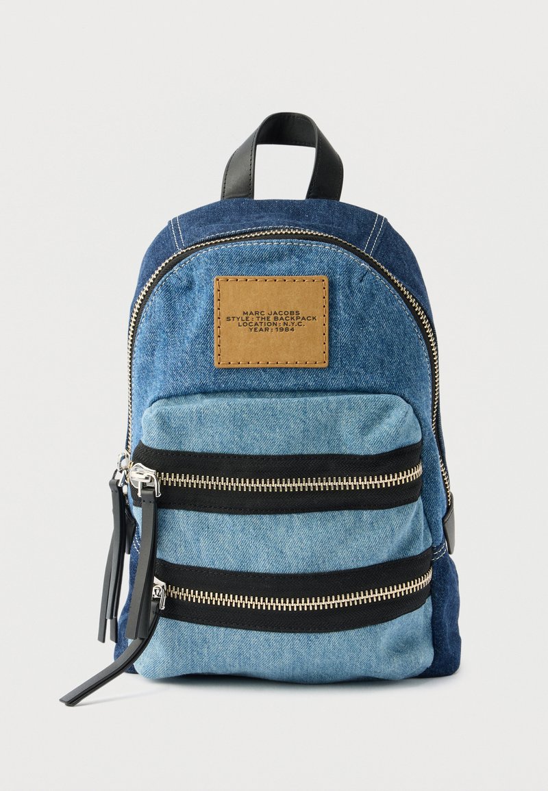 Μικρό δίχρωμο μπλε τζιν σακίδιο πλάτης με δύο εμπρόσθιες τσέπες με φερμουάρ και καφέ ετικέτα στο επάνω εμπρόσθιο πάνελ.