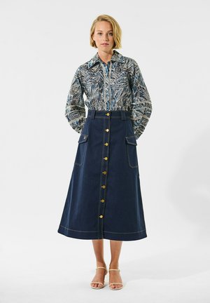 Blau-beige gestreifte Bluse mit floralem Muster, kombiniert mit einem dunkelblauen A-Linien-Rock aus Denim mit goldenen Knöpfen und aufgesetzten Taschen.