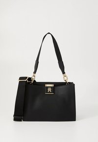 Musta käsilaukku, valmistettu kuorekkkaisesta nahasta ja muotoiltu rakenteellisesti. Varustettu kultaisin metalliosin ja irrotettavalla hihnalla, jossa on teksturoitua yksityiskohtaa.