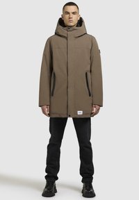 Brun isoleret parka med hætte, der har lynlåslommer og en afslappet pasform. Struktureret stof med en mat finish, kombineret med sorte detaljer.