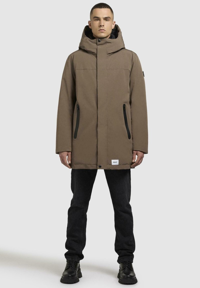 Brun isoleret parka med hætte, der har lynlåslommer og en afslappet pasform. Struktureret stof med en mat finish, kombineret med sorte detaljer.