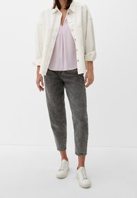 Giacca di jeans oversize color beige chiaro sopra un top rosa pallido, abbinata a jeans grigi a sigaretta e sneaker bianche con suole testurizzate.