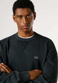Felpa di un blu navy scuro realizzata in cotone, con scollo rotondo a coste, maniche lunghe e un piccolo logo ricamato "PJL" sul petto.