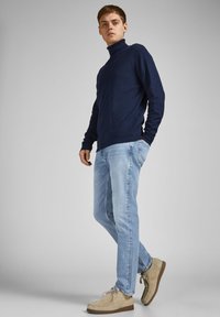 Navy turtleneck sweater, light blue jeans, and beige lace-up shoes. Soft texture, fitted design with long sleeves and casual style.