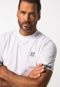 Valkoinen T-paita pyöreällä kauluksella, jossa on musta teksti "J π" rinnassa ja "GERMANY" hihassa. Pehmeä kangas, vartalonmyötäinen malli.