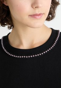 Maglione nero con scollatura rotonda decorata da piccole perline viola simili a perle e cuciture texturizzate, che evidenziano i suoi dettagli decorativi.