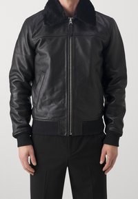 Svart läderbomberjacka med en shearlingkrage, ribbade manschetter och fåll, dragkedjestängning och sidofickor som ger en strukturerad form.