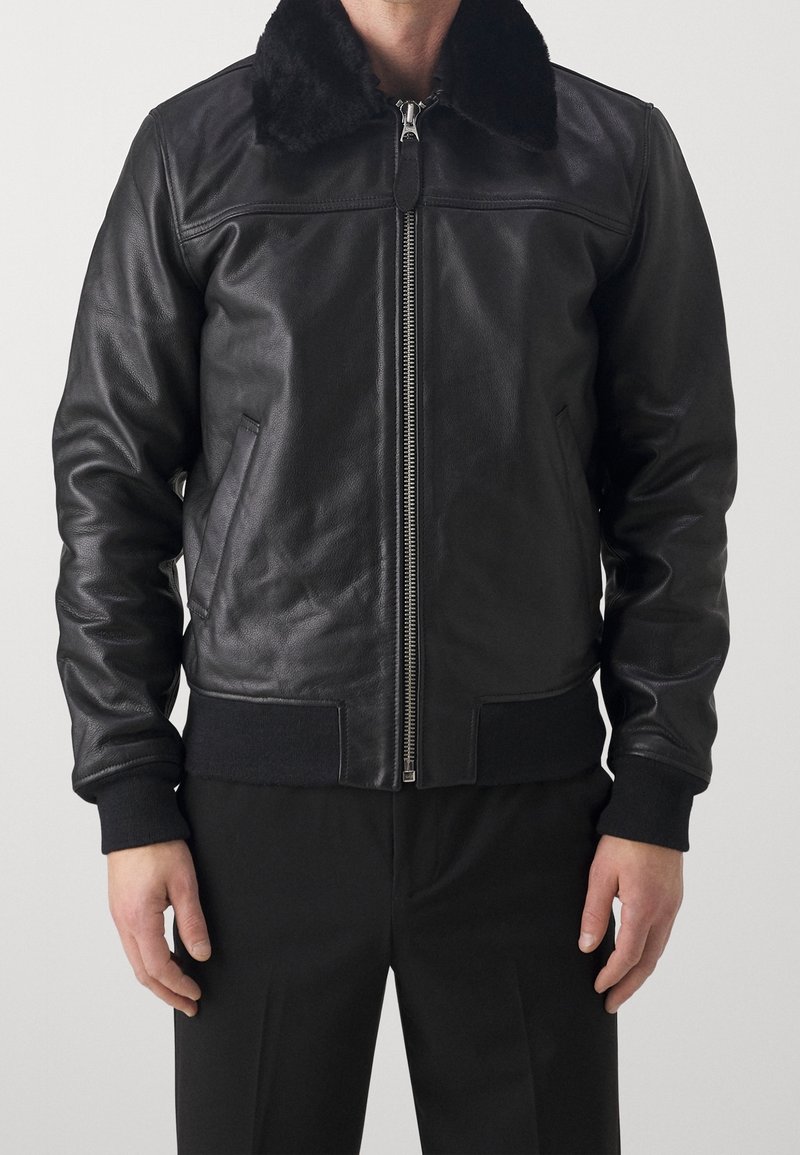 Svart läderbomberjacka med en shearlingkrage, ribbade manschetter och fåll, dragkedjestängning och sidofickor som ger en strukturerad form.