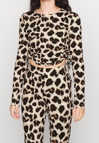 Długi rękaw top wykonany z miękkiego materiału, z beżową bazą i czarno-brązowym wzorem w panterkę, z marszczeniami po bokach i regulowanymi sznurkami.